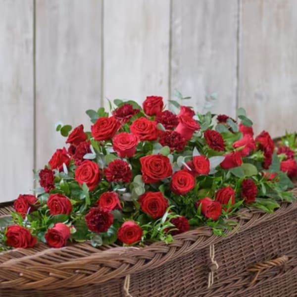 Red roses and carnations arranged in a wicker casket spray