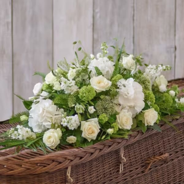 White and green floral arrangement on a wicker casket