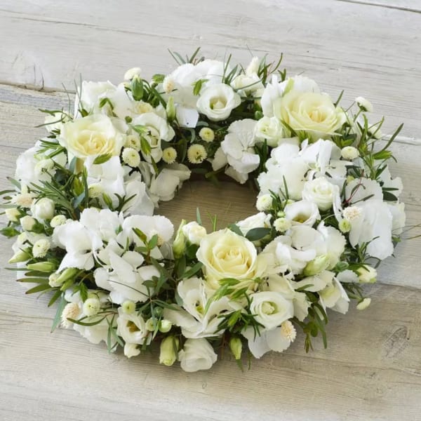 White floral wreath with roses and small blooms on a wood surface