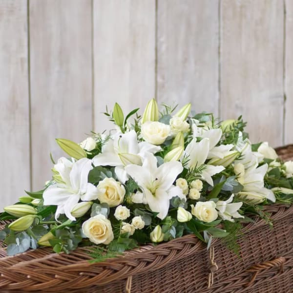 White lilies and cream roses arranged in a wicker casket spray