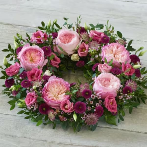 Pink and magenta floral wreath with large roses on a wood surface