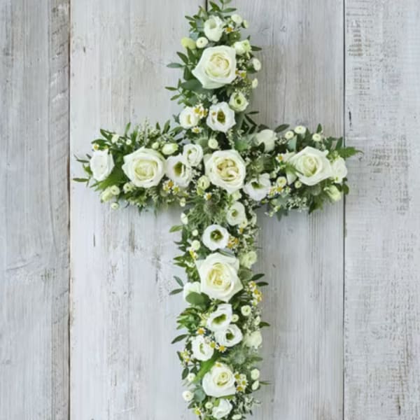 White floral cross covered in roses and small blooms on a wood background