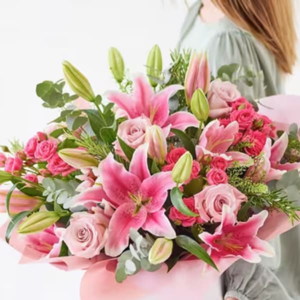 Pink lilies and roses arranged in a bouquet with green foliage