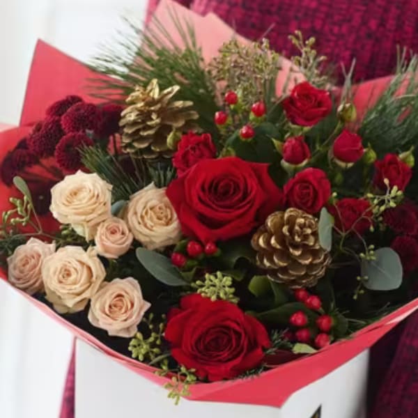 Bouquet of red and cream roses with gold pinecones in pink wrapping
