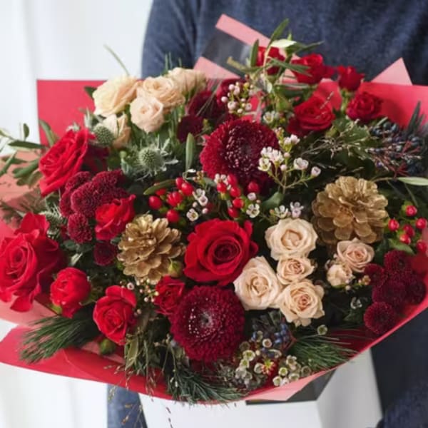 Bouquet of red and cream roses with pinecones and greenery in pink wrap