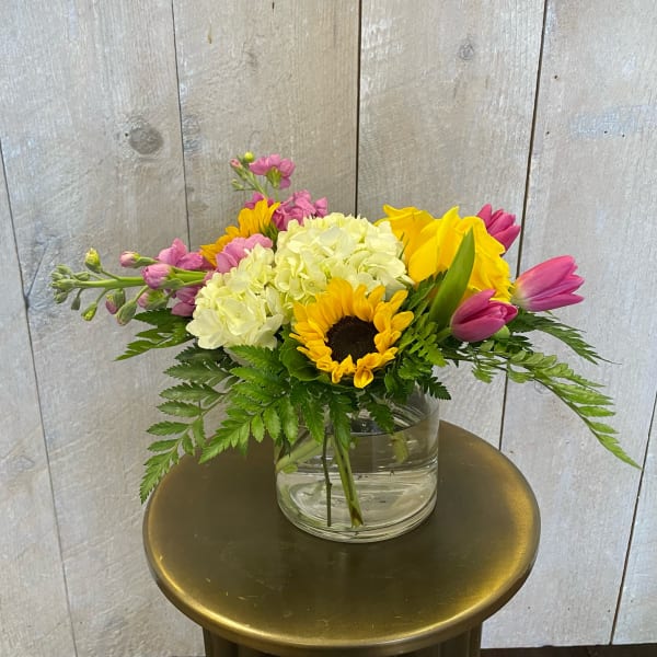 Mixed bouquet with sunflowers, hydrangeas, tulips, and pink stock in a glass vase