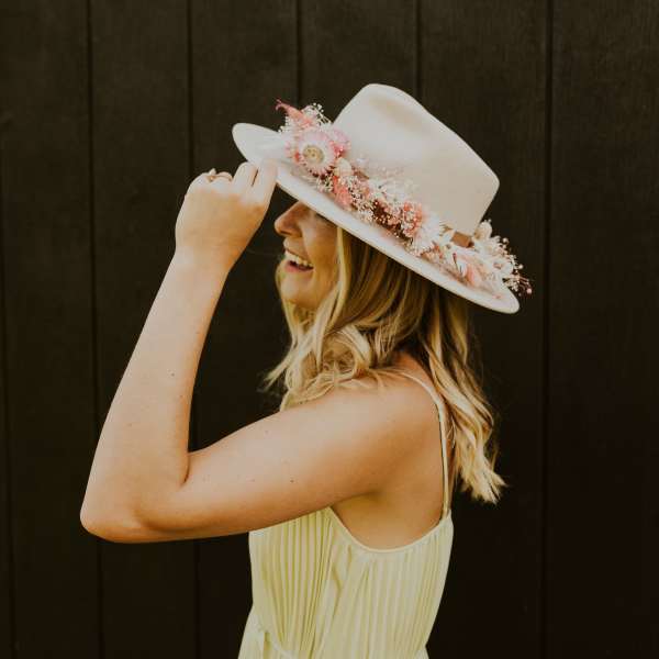 Woman in a light dress wearing a cream hat decorated with pink and white flowers around the crown