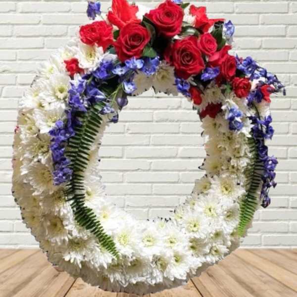 Large floral wreath with red roses, white daisies, and blue flowers