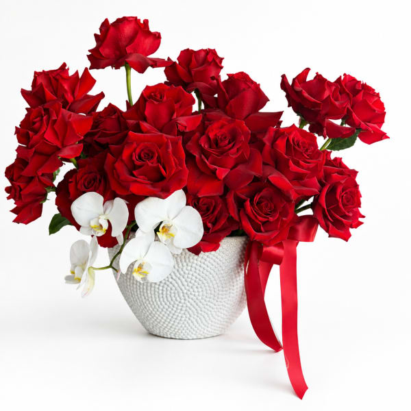Red roses and white orchids in a white textured vase with a red ribbon