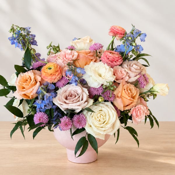 Mixed bouquet of roses, ranunculus, and blue flowers in a pink vase