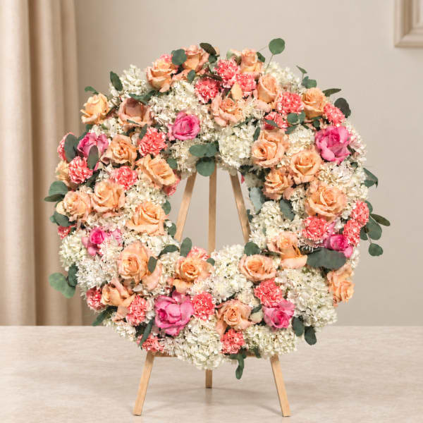 Floral wreath on a wooden easel with peach, pink, and white blooms