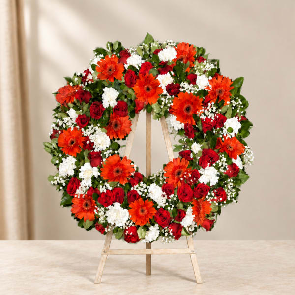 Circular wreath of red, white, and orange flowers on a wooden easel