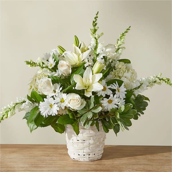 White floral arrangement in a woven basket with lilies, roses, and daisies
