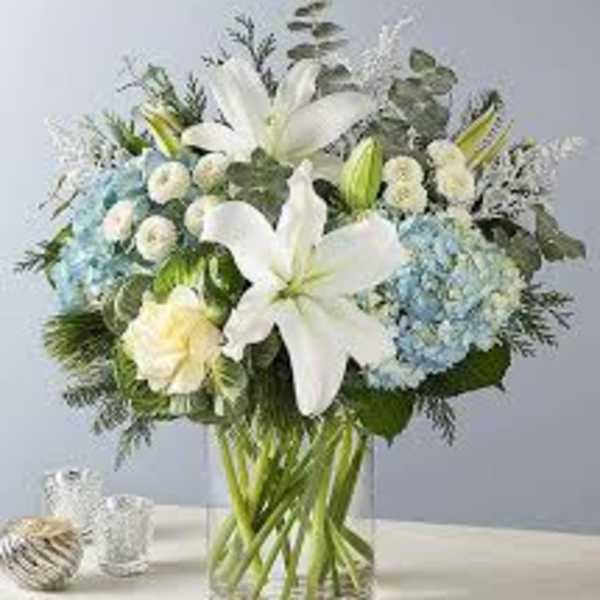 White lilies and blue hydrangeas in a clear glass vase