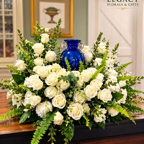 White roses arranged around a cobalt blue vase with greenery