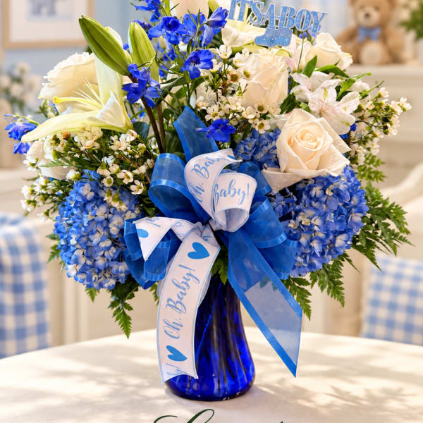 Blue and white flower arrangement in a vase with baby-themed ribbons