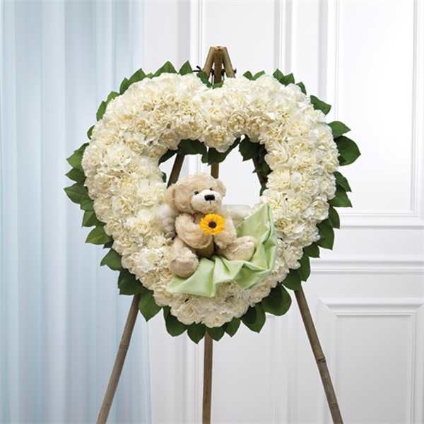 Heart-shaped white floral wreath with a teddy bear and ribbon on an easel