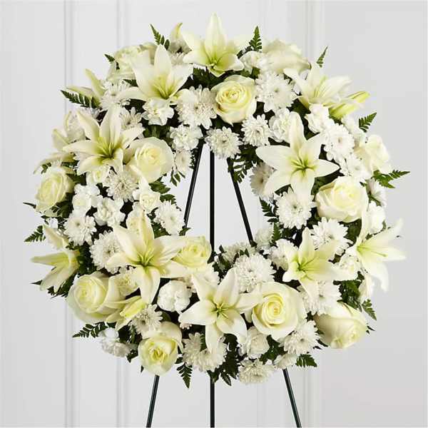 White floral wreath on a black stand with roses and lilies