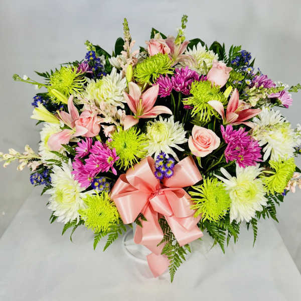 Mixed bouquet with pink lilies, roses, and white and green chrysanthemums tied with a pink ribbon