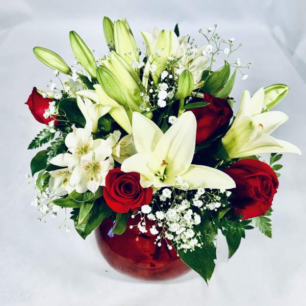 Bouquet of white lilies and red roses in a red glass vase