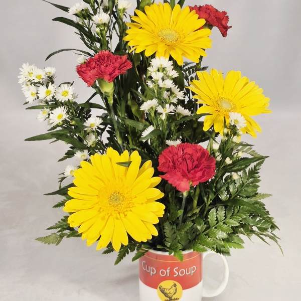 Mixed yellow and red flowers arranged in a mug labeled Get Well