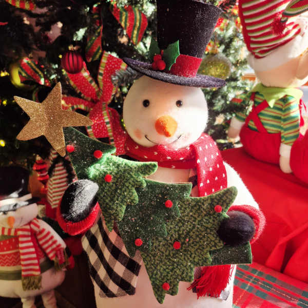 Decorative snowman figurine with a top hat and scarf in front of a Christmas tree