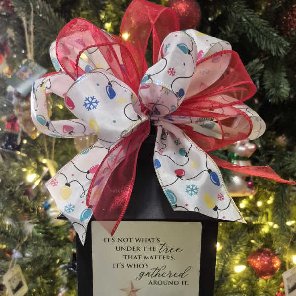 Black lantern with a Christmas ribbon bow and holiday card in front of a decorated tree