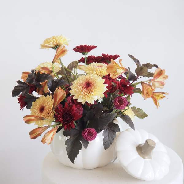Mixed flowers arranged in a white pumpkin-shaped vase with a lid beside it