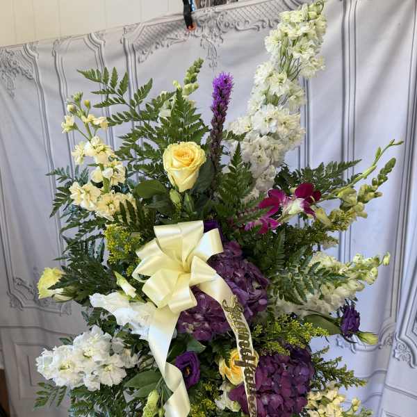 Standing floral spray with white, purple, and yellow blooms and a cream ribbon