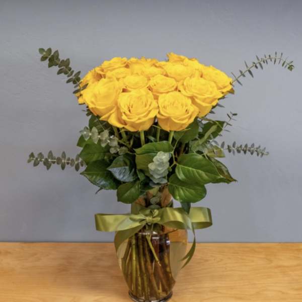 Yellow roses arranged in a glass vase with a green ribbon