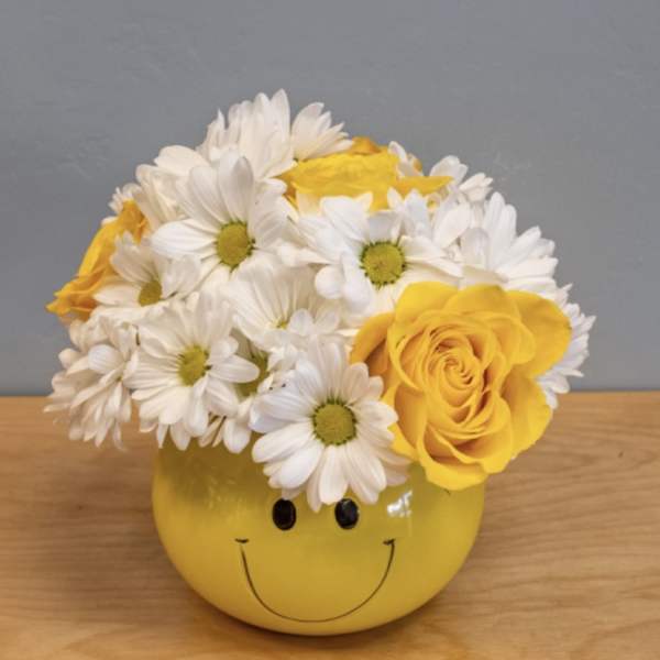 Yellow smiley-face vase holding white daisies and yellow roses