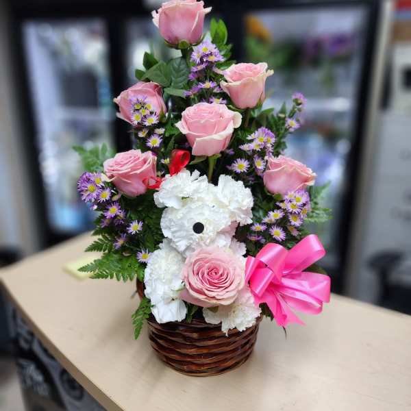Pink roses and white carnations in a wicker basket with a pink bow