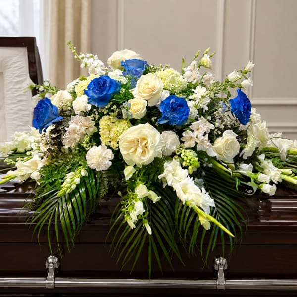 Large blue, white, and cream floral casket spray on a dark coffin