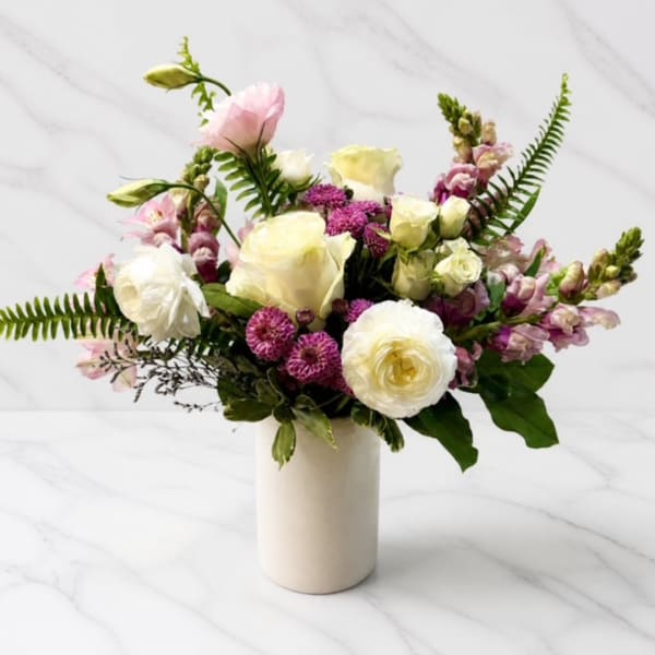 Mixed bouquet of white, cream, pink, and purple flowers in a white vase