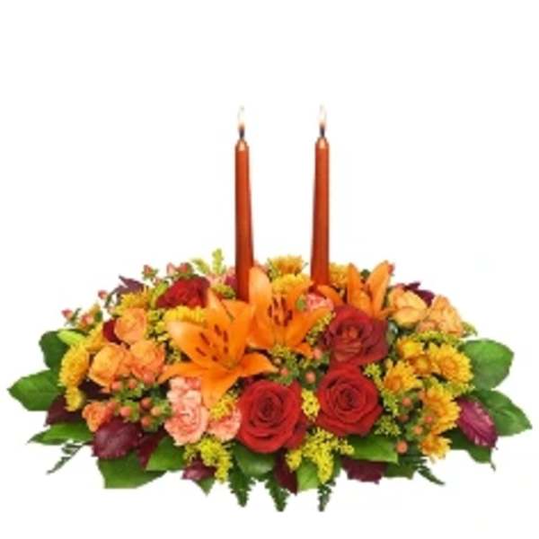 Low floral centerpiece with two orange candles and mixed blooms