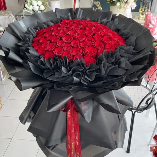 Large bouquet of red roses wrapped in black paper with a red ribbon