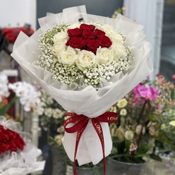 Red and white rose bouquet wrapped in white paper with a red ribbon
