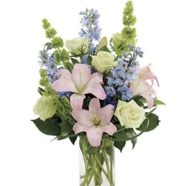 Bouquet of pink lilies, white roses, and blue flowers in a clear glass vase