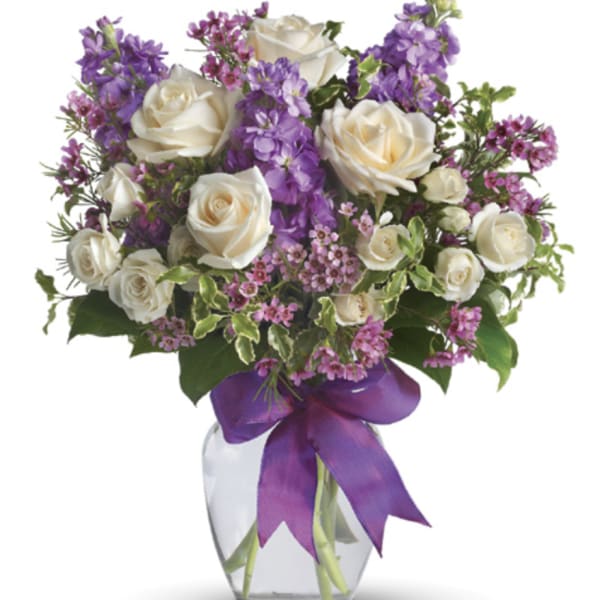 Mixed bouquet of white roses and purple flowers in a glass vase with a purple bow