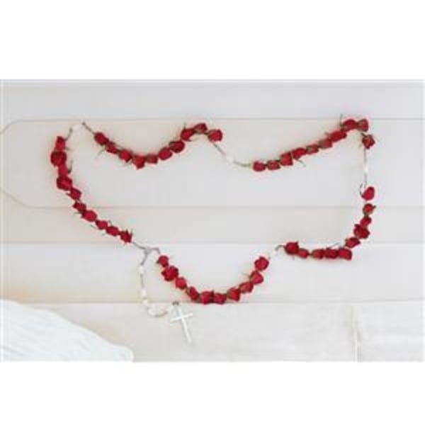 Red rose garland draped across a white headboard with a small cross pendant