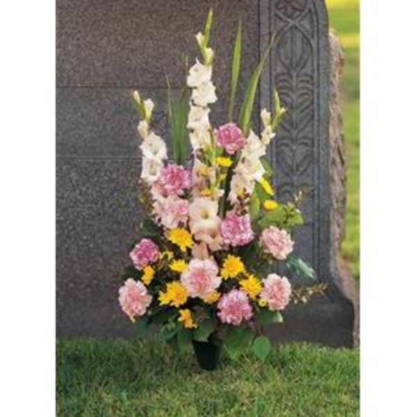 Standing funeral spray with pink and yellow flowers beside a gravestone