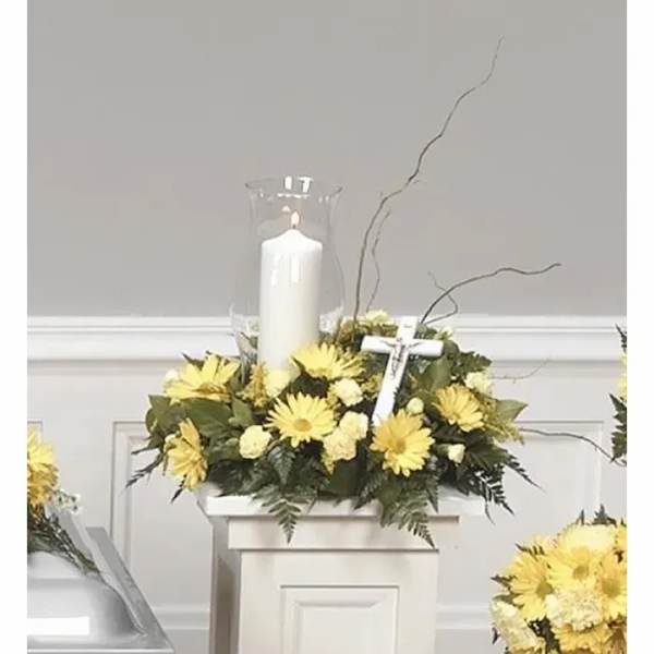 Yellow floral arrangement with a white candle in a glass hurricane