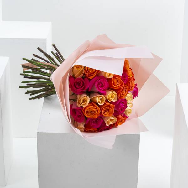 Bouquet of orange and pink roses wrapped in pale pink paper