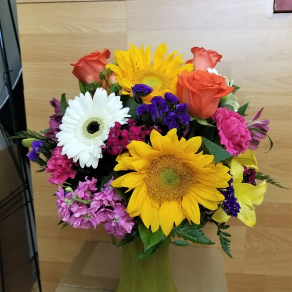 Colorful bouquet with sunflowers, roses, and daisies in a green vase