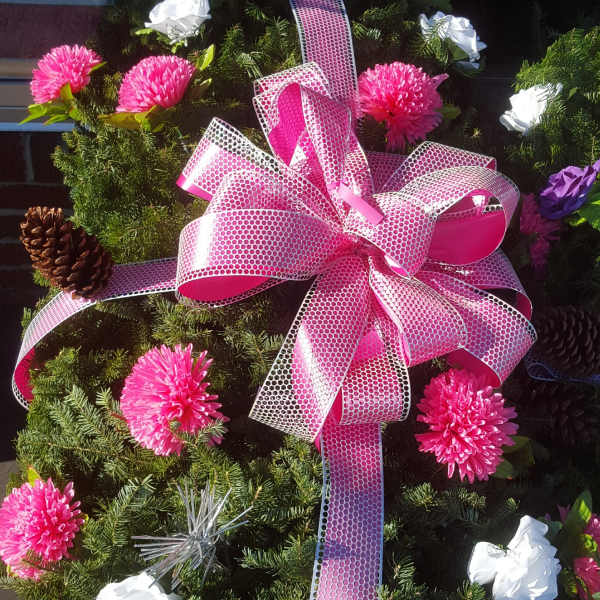 Evergreen wreath with pink ribbon, pink and white flowers, and pinecones