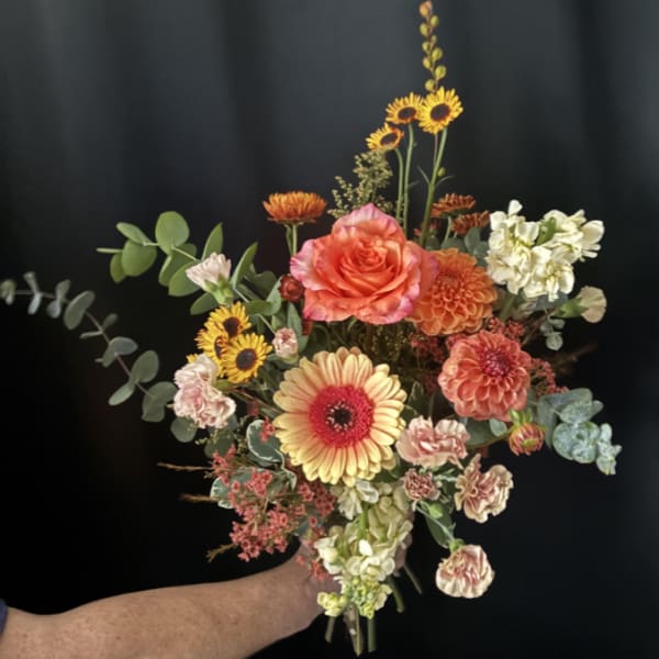 Handheld bouquet with orange and yellow flowers against a dark background.