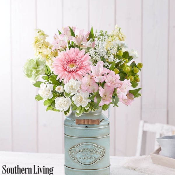 Pink and white flowers arranged in a blue metal vase on a table.