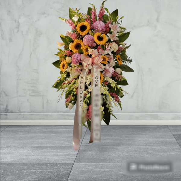 Standing floral spray with sunflowers, pink blooms, and ribbon streamers