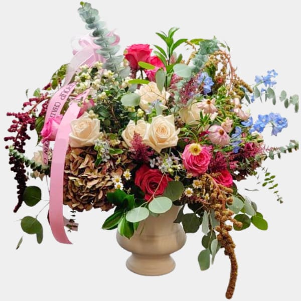 Mixed bouquet of roses and wildflowers in a beige vase with pink ribbon