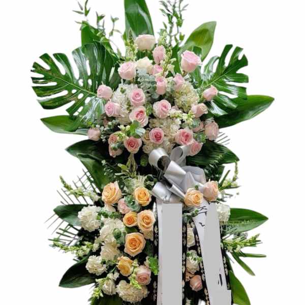 Tall standing floral spray with pink and peach roses and large tropical leaves
